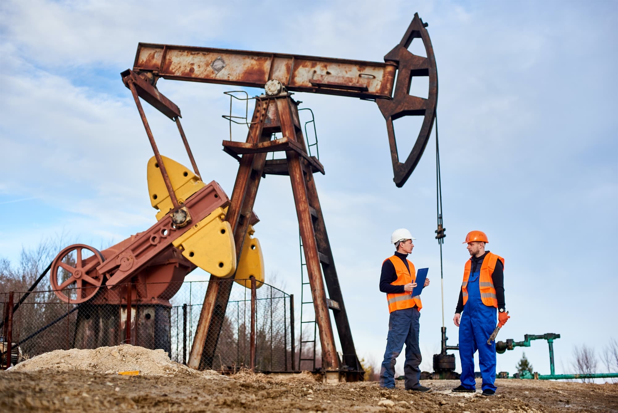 PelicanSoft - Two workers standing in front of an oil pump, performing database administration for EvalPro.